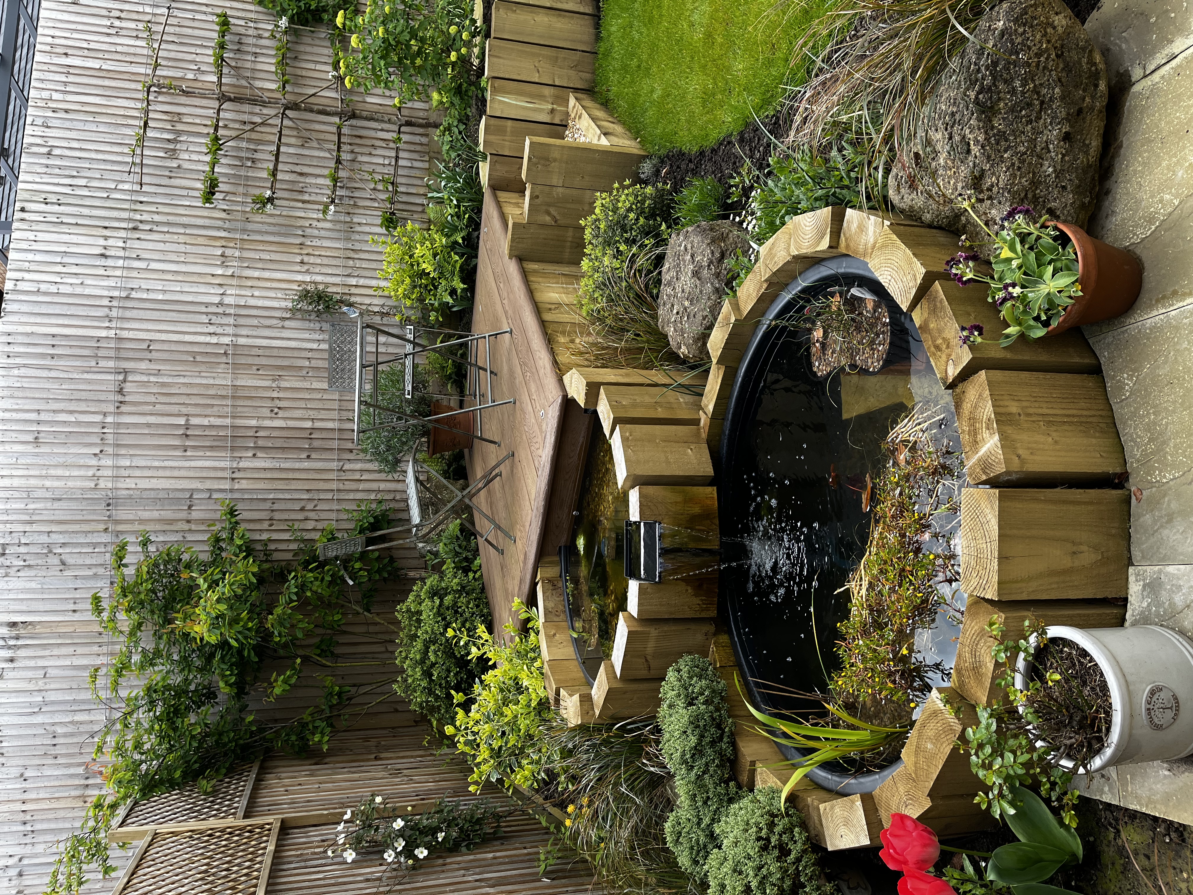 New-build garden terrace with raised timber decking, a tiered pond and layered structural planting